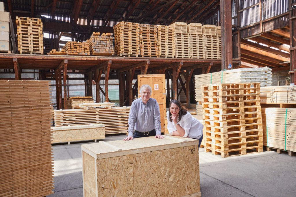 Team der Ernst Müller GmbH in der Lagerhalle zwischen Paletten und Holzkisten
